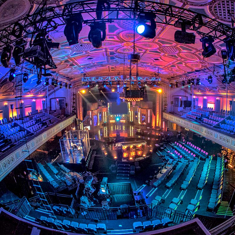 broadcast-events An expansive auditorium with a prominent stage illuminated by lights, offering ample seating for an audience.